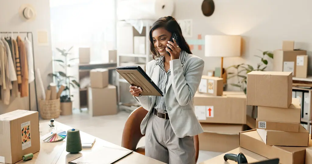 Woman using phone and a tablet to manage logistics of her store.